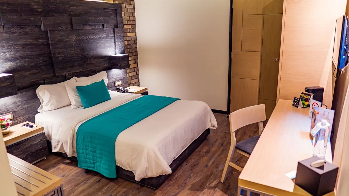 Deluxe Room with a queen bed at Hotel Punto MX. A work desk and coffee maker are visible.