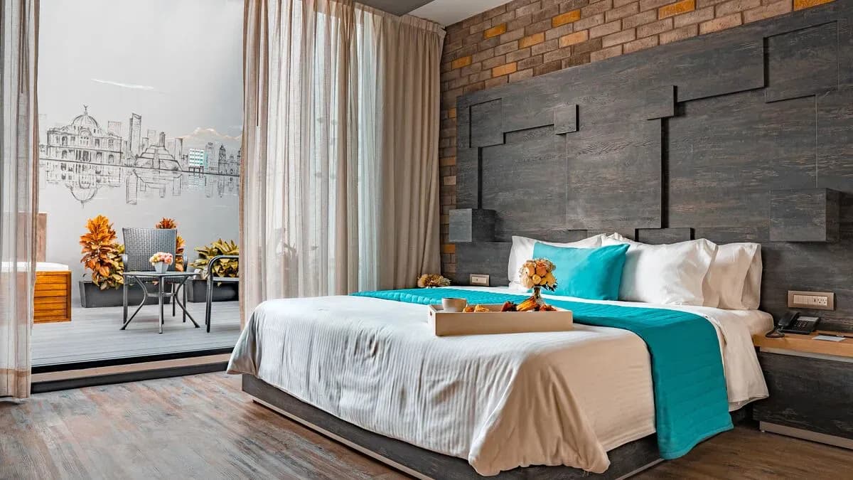 Suite Master de l'Hôtel Punto MX avec une baignoire en arrière-plan et une table avec des chaises. Fresque de la ville de Mexico sur le mur. Un plateau de petit déjeuner est sur le lit.