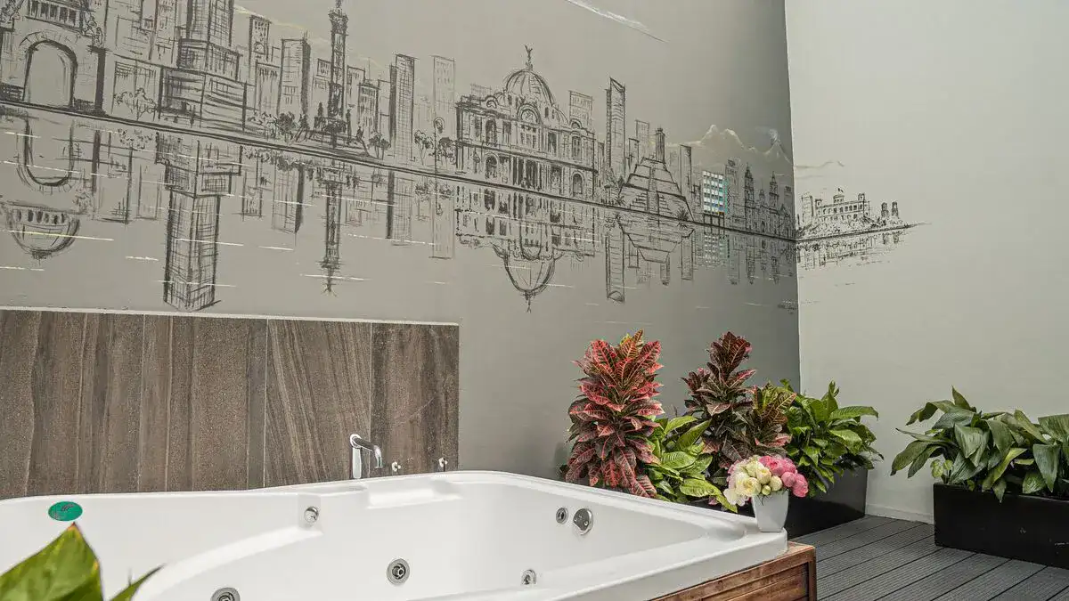 Baignoire dans la Suite Master de l'Hôtel Punto MX avec fresque de la ville de Mexico sur le mur et des plantes sur le sol.